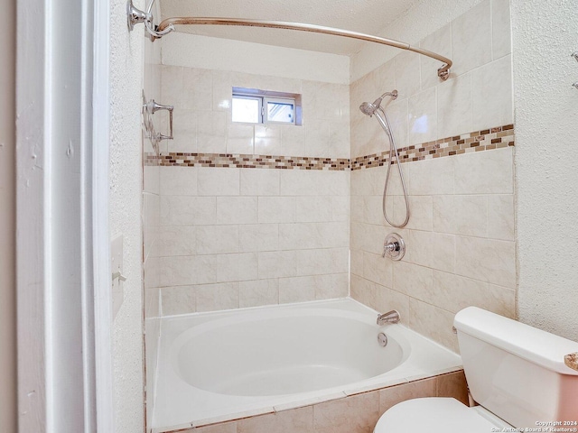 bathroom with a textured ceiling, toilet, and tiled shower / bath combo