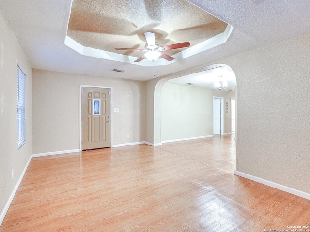 spare room featuring a raised ceiling, ceiling fan with notable chandelier, light hardwood / wood-style floors, and a textured ceiling