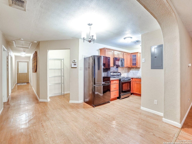 kitchen featuring electric panel, black appliances, hanging light fixtures, light wood-type flooring, and a textured ceiling