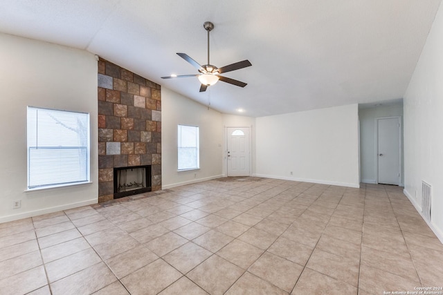 unfurnished living room with a tiled fireplace, a wealth of natural light, ceiling fan, and vaulted ceiling