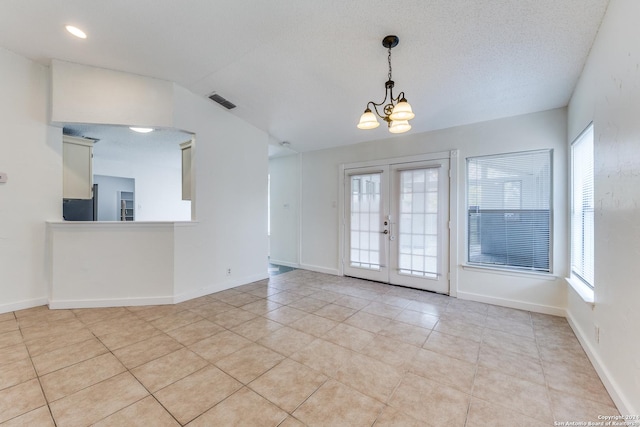 tiled spare room with a textured ceiling, a wealth of natural light, and a notable chandelier