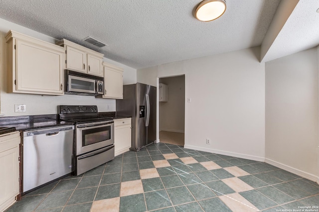 kitchen with appliances with stainless steel finishes, a textured ceiling, dark tile patterned flooring, and cream cabinets