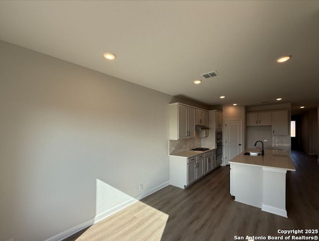 kitchen featuring a center island with sink, backsplash, gas stovetop, dark hardwood / wood-style flooring, and sink