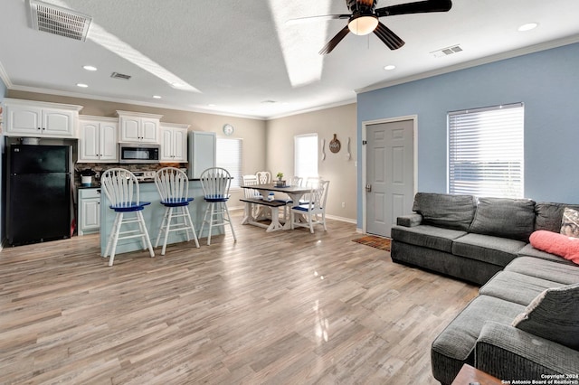 living room with ceiling fan, a healthy amount of sunlight, light hardwood / wood-style floors, and ornamental molding