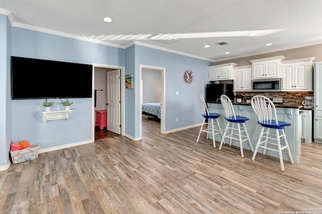 kitchen featuring a kitchen breakfast bar, white cabinetry, stainless steel appliances, and light hardwood / wood-style flooring