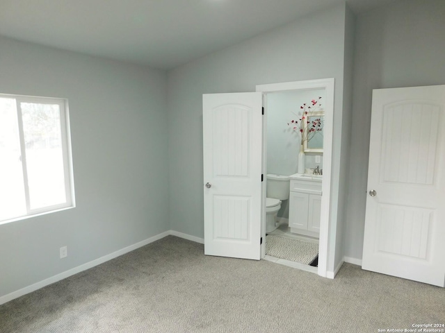 unfurnished bedroom featuring ensuite bathroom, sink, light colored carpet, and vaulted ceiling