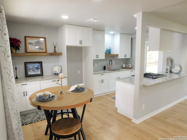 kitchen featuring light wood-type flooring, light stone counters, stainless steel gas cooktop, sink, and white cabinets