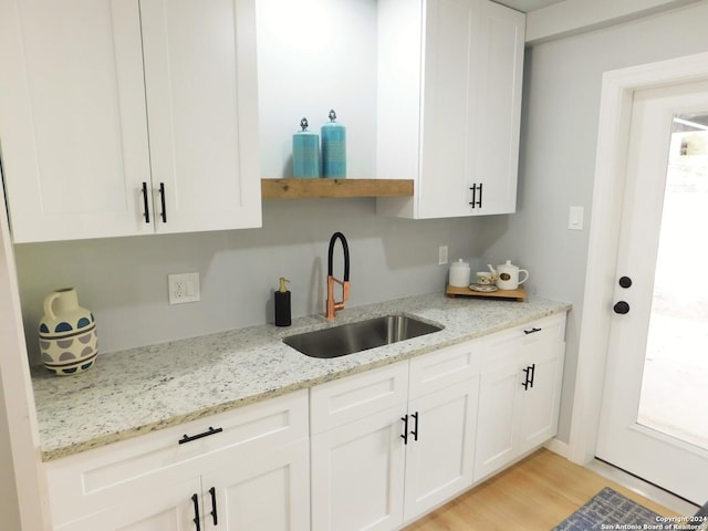 kitchen with light hardwood / wood-style floors, light stone countertops, white cabinetry, and sink