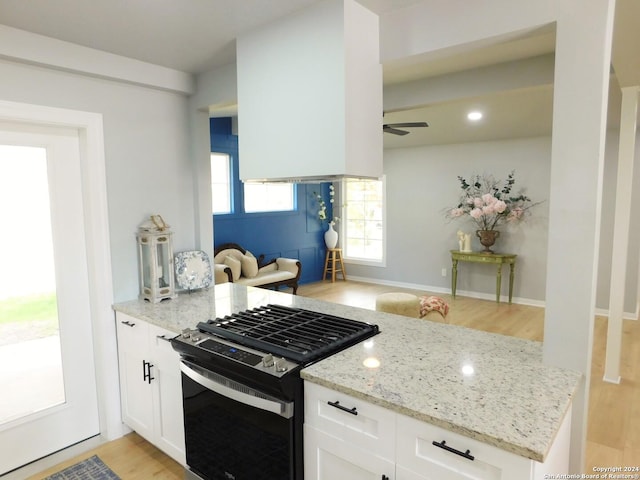 kitchen with light stone countertops, light hardwood / wood-style floors, white cabinetry, and black range