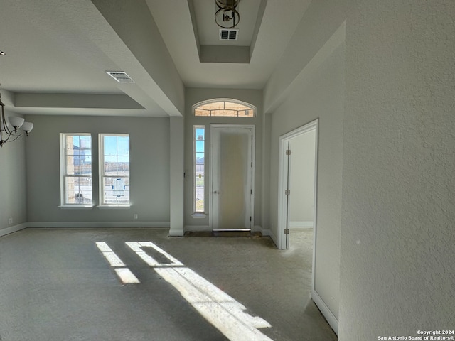 carpeted foyer entrance featuring a tray ceiling and an inviting chandelier