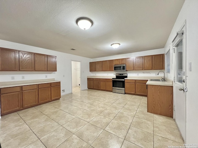 kitchen featuring light tile patterned floors, a textured ceiling, stainless steel appliances, and sink