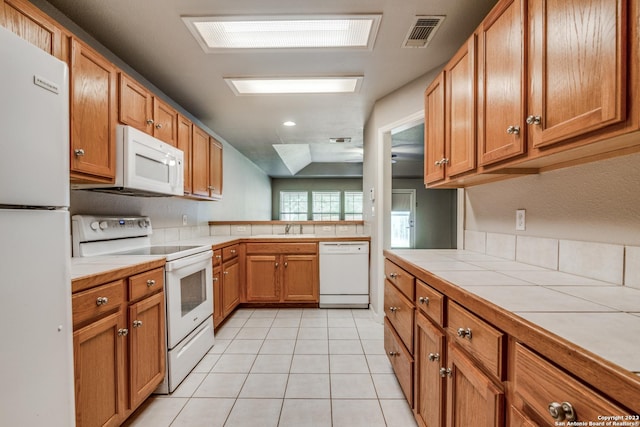 kitchen featuring white appliances, sink, a skylight, light tile patterned floors, and tile counters