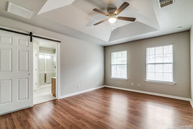 spare room featuring light wood-type flooring, a textured ceiling, a raised ceiling, ceiling fan, and a barn door