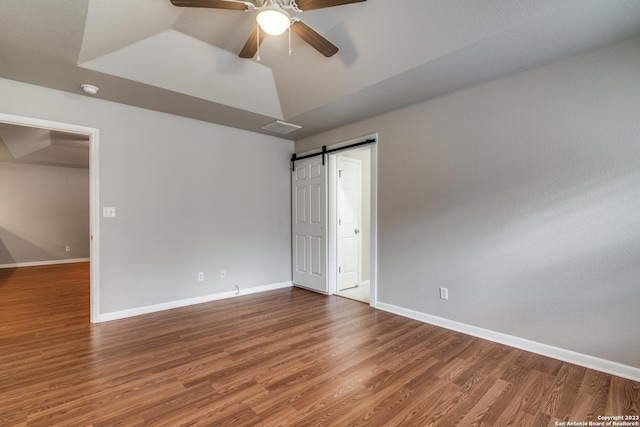 unfurnished room featuring a barn door, ceiling fan, and hardwood / wood-style flooring