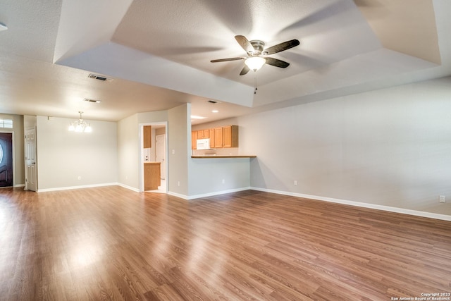 unfurnished living room with wood-type flooring, ceiling fan with notable chandelier, and a raised ceiling