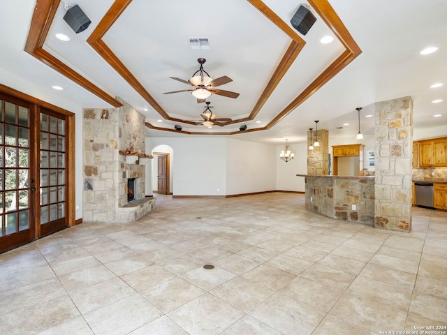 unfurnished living room featuring french doors, ceiling fan with notable chandelier, a stone fireplace, a raised ceiling, and crown molding