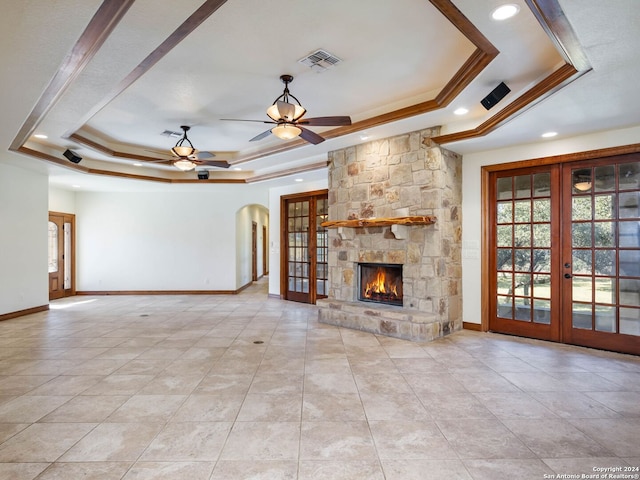 unfurnished living room featuring french doors, ornamental molding, a raised ceiling, ceiling fan, and a fireplace