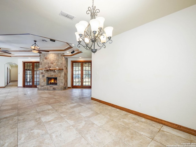 unfurnished living room with french doors, a raised ceiling, a stone fireplace, crown molding, and ceiling fan with notable chandelier