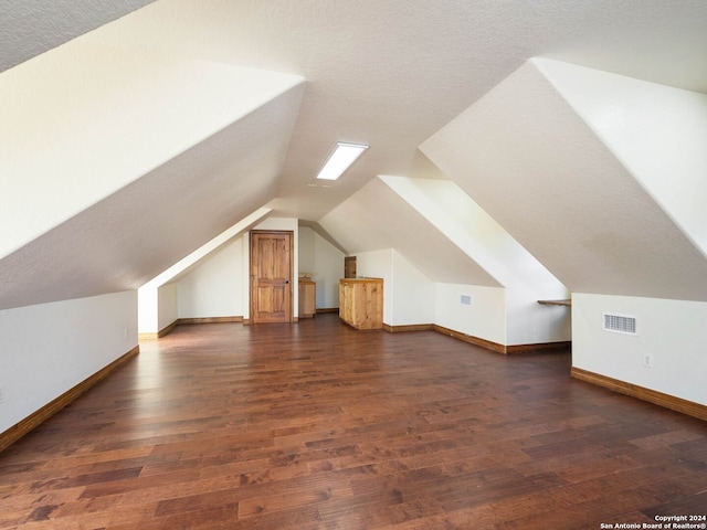 bonus room with a textured ceiling, lofted ceiling, and dark wood-type flooring