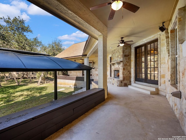 view of patio with an outdoor stone fireplace, french doors, and ceiling fan