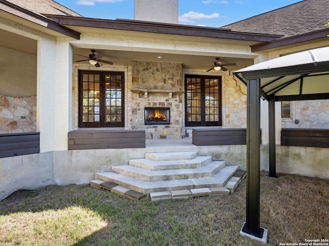 view of exterior entry featuring an outdoor stone fireplace and ceiling fan