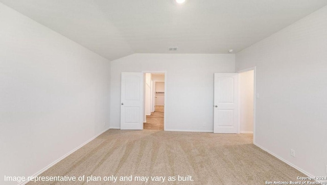 unfurnished bedroom with light colored carpet, a walk in closet, and vaulted ceiling