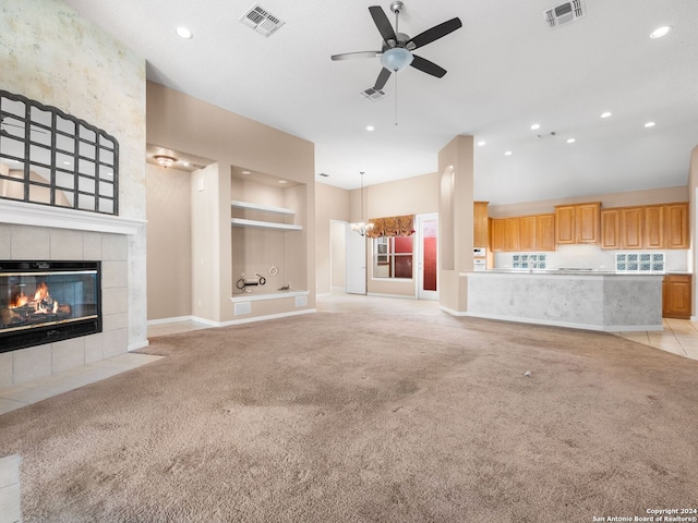 unfurnished living room featuring ceiling fan with notable chandelier, light carpet, and a tile fireplace