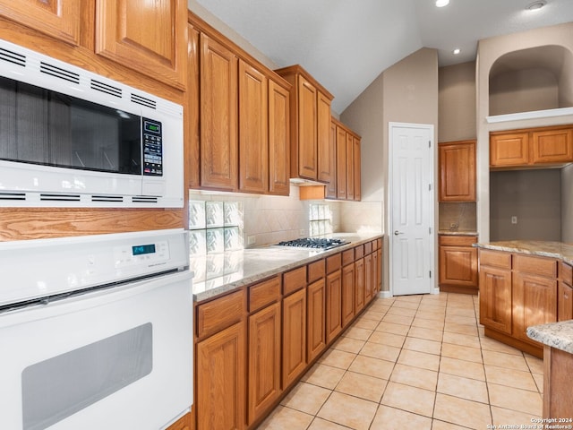 kitchen with light stone countertops, decorative backsplash, stainless steel appliances, lofted ceiling, and light tile patterned flooring