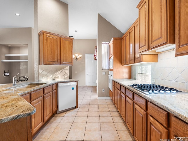 kitchen featuring sink, light stone counters, a chandelier, white appliances, and decorative light fixtures