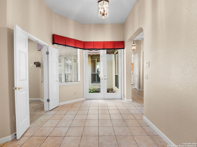 hall with a chandelier, french doors, and light tile patterned flooring