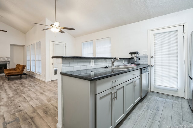 kitchen with a fireplace, vaulted ceiling, sink, light hardwood / wood-style flooring, and dishwasher