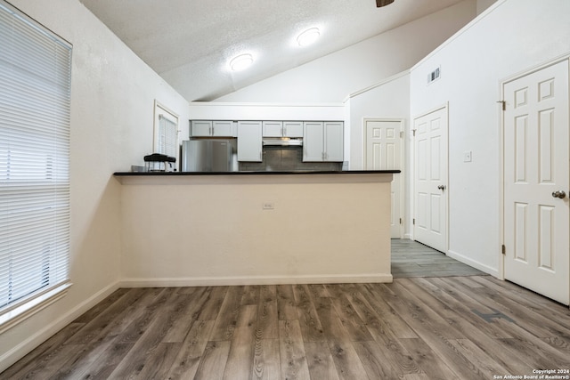 kitchen with kitchen peninsula, stainless steel fridge, dark wood-type flooring, and gray cabinetry