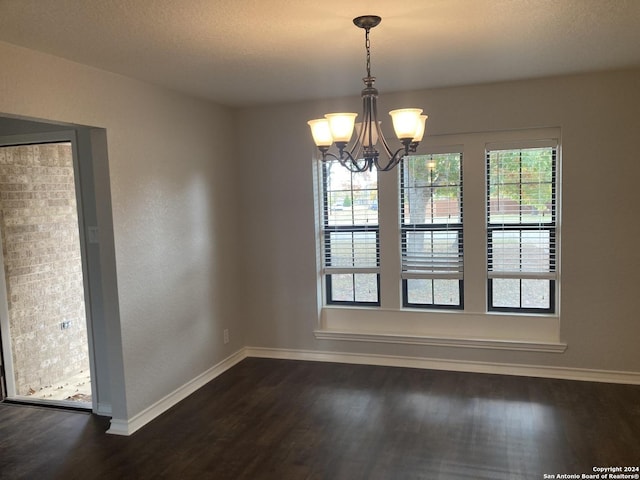 unfurnished dining area featuring dark hardwood / wood-style flooring, a textured ceiling, and a chandelier