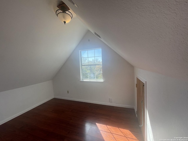 additional living space featuring a textured ceiling, dark hardwood / wood-style flooring, and lofted ceiling