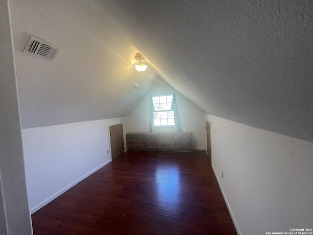 additional living space with a textured ceiling, dark wood-type flooring, and lofted ceiling