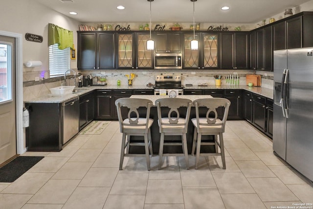 kitchen with decorative light fixtures, a center island, sink, stainless steel appliances, and light stone counters