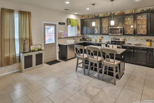 kitchen featuring a center island, hanging light fixtures, a breakfast bar area, stainless steel appliances, and light stone counters