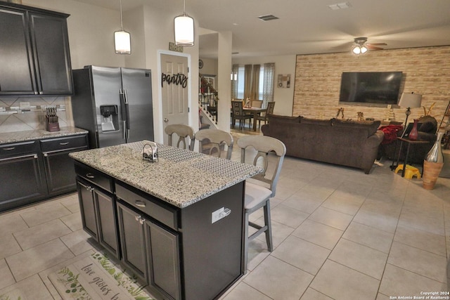 kitchen featuring stainless steel fridge, ceiling fan, a kitchen island, pendant lighting, and a breakfast bar