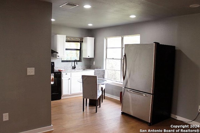 kitchen featuring sink, light hardwood / wood-style flooring, black / electric stove, stainless steel fridge, and white cabinets