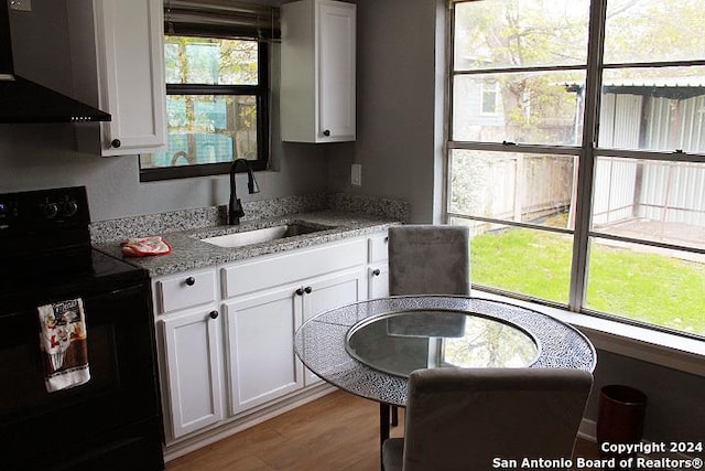 kitchen featuring light stone countertops, ventilation hood, sink, black electric range, and white cabinetry