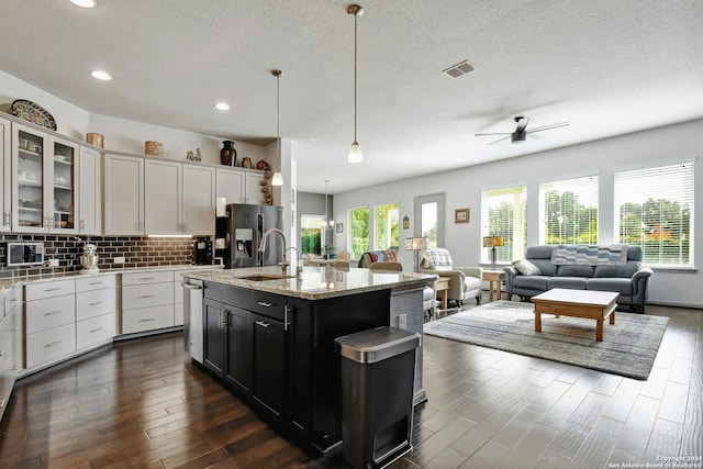 kitchen featuring a center island with sink, white cabinets, hanging light fixtures, and a wealth of natural light