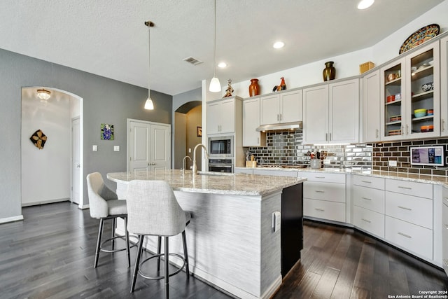 kitchen featuring appliances with stainless steel finishes, dark wood-type flooring, sink, a center island with sink, and hanging light fixtures