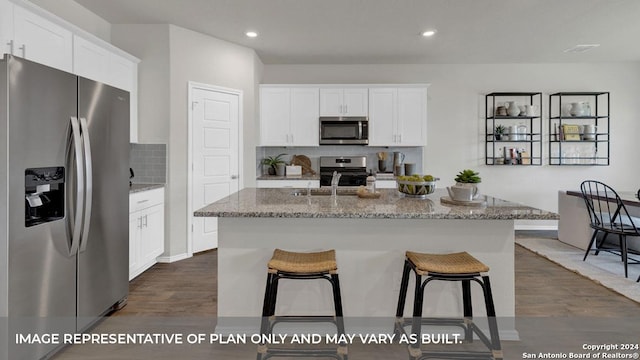 kitchen with white cabinetry, light stone countertops, dark wood-type flooring, stainless steel appliances, and an island with sink