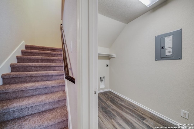 stairs featuring hardwood / wood-style flooring, lofted ceiling, a textured ceiling, and electric panel