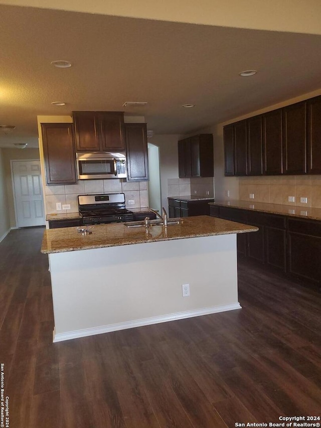 kitchen with dark wood-type flooring, sink, an island with sink, light stone counters, and stainless steel appliances