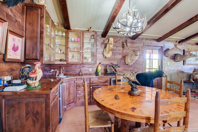 kitchen with beamed ceiling, sink, an inviting chandelier, and wood walls