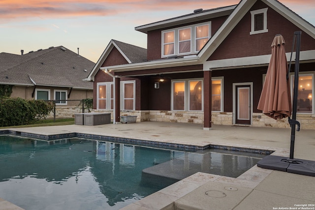 back house at dusk featuring a pool with hot tub and a patio