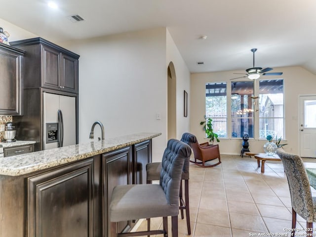 kitchen featuring stainless steel fridge, dark brown cabinetry, light tile patterned floors, and vaulted ceiling