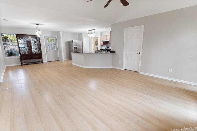 unfurnished living room with ceiling fan with notable chandelier and light hardwood / wood-style floors