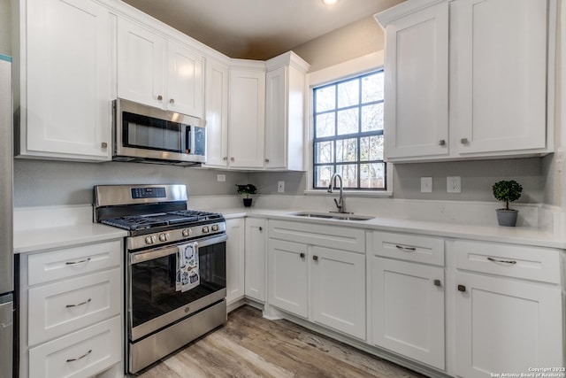 kitchen with light wood-type flooring, stainless steel appliances, sink, and white cabinets